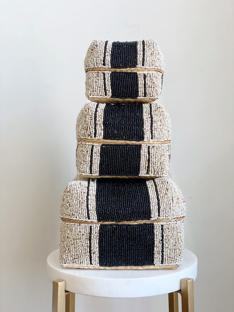 set of three hand-beaded black and tan bamboo baskets on a white marble stool