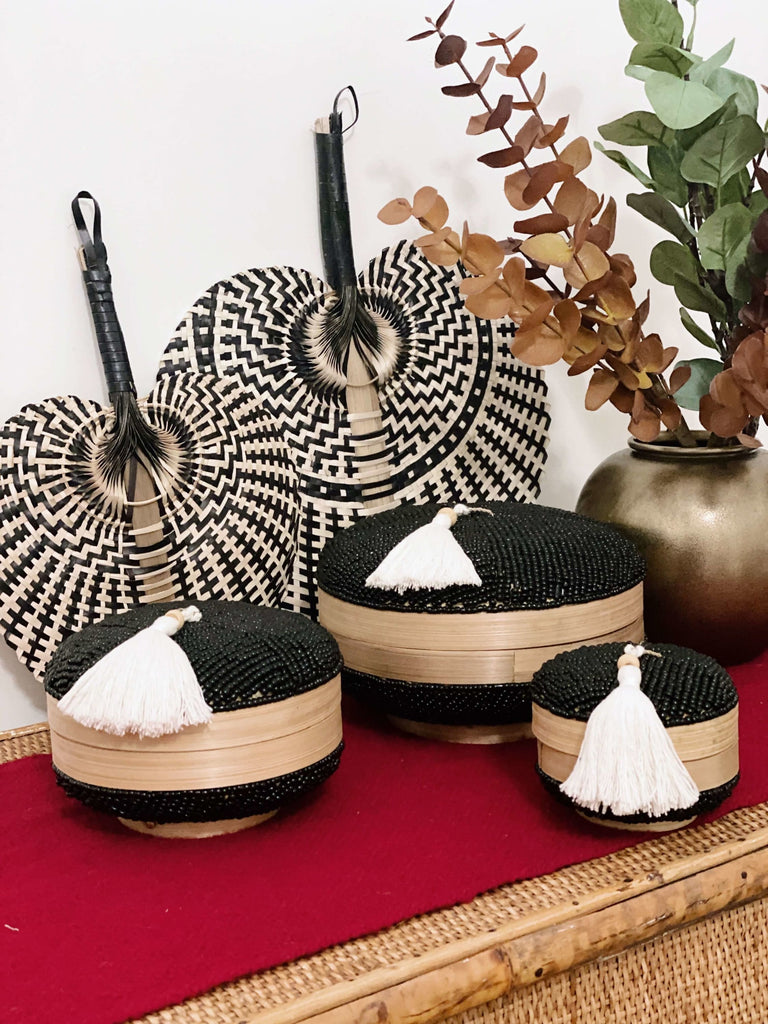 trio set of round hand-beaded black bamboo baskets on table with a double set of palm leaf fans