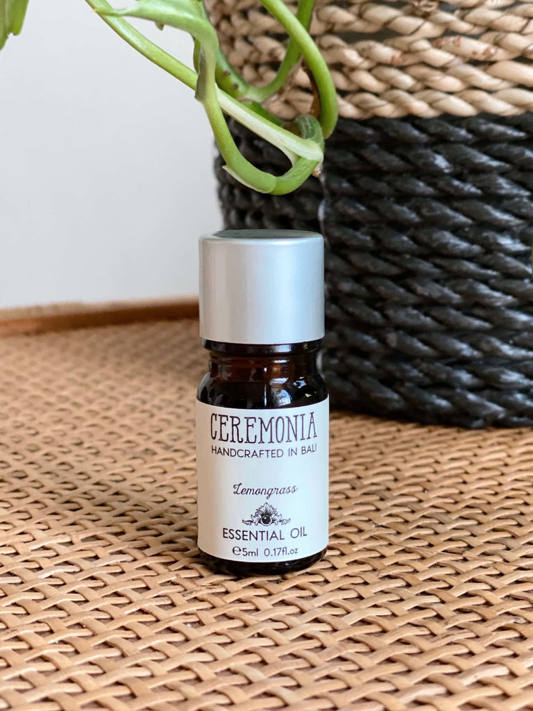 CEREMONIA lemongrass essential oil in front of a black and brown woven plant pot on a wicker dresser