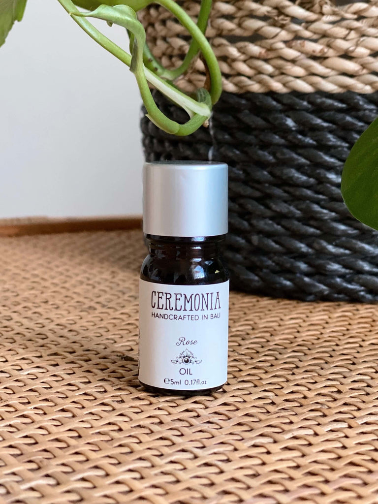 CEREMONIA rose essential oil in front of a black and brown woven plant pot on a wicker dresser