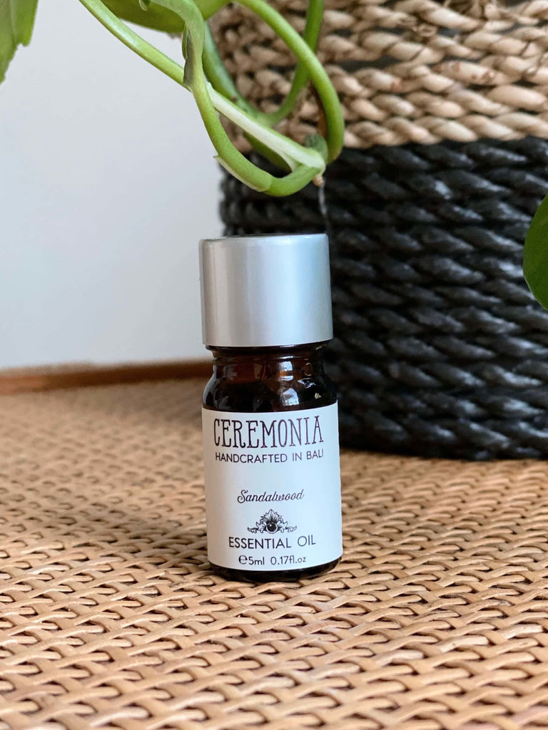 CEREMONIA sandalwood essential oil in front of a black and brown woven plant pot on a wicker dresser