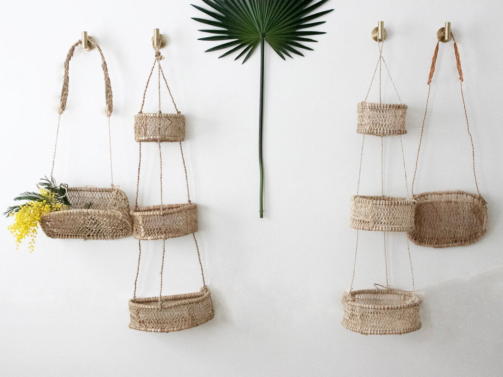two single cottagecore wall baskets and two trio bohemian wall baskets hanging on white wall with palm leaf