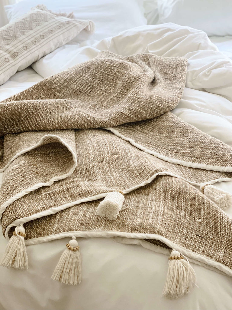 bohemian handwoven jute and linen cream cozy throw blanket with tassels on a white bedding