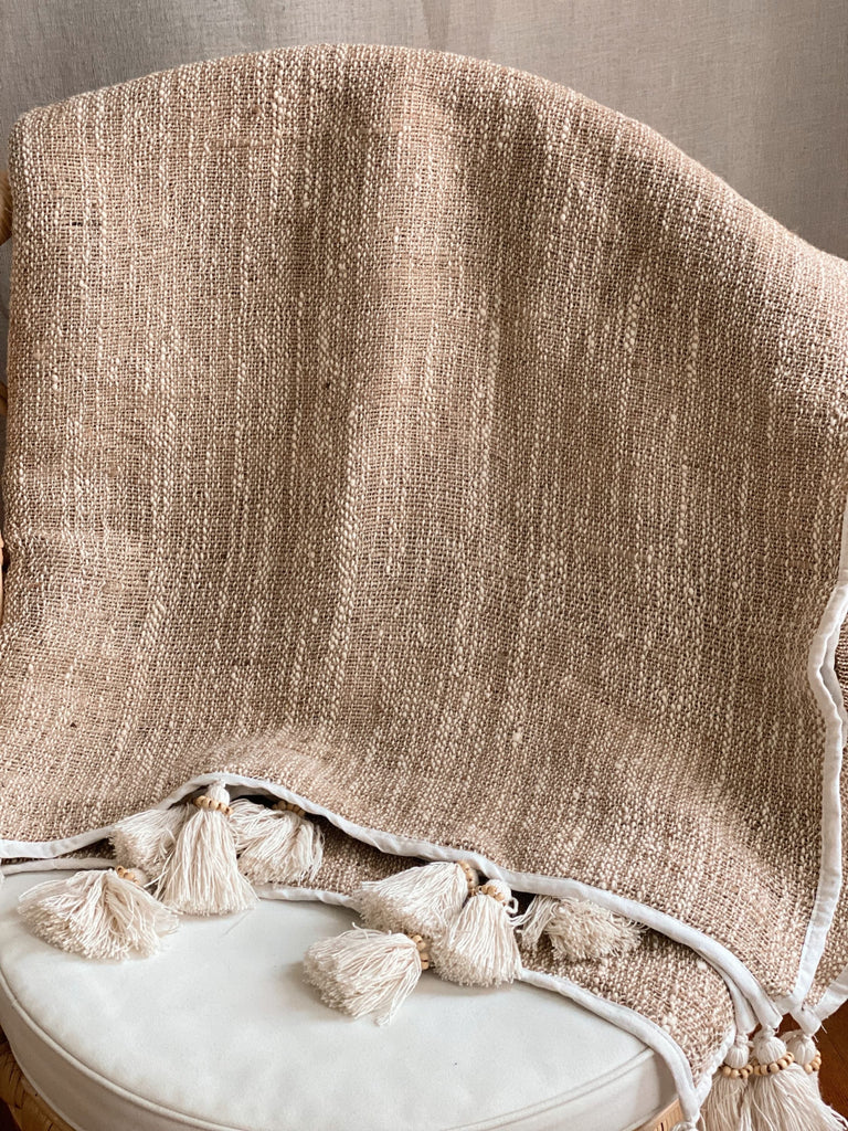 scandi bohemian jute and linen throw blanket with cream tassels over a wicker chair