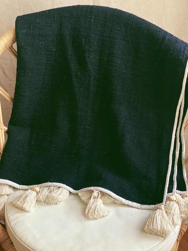 dark bohemian black jute and linen throw blanket with cream tassels over a wicker chair