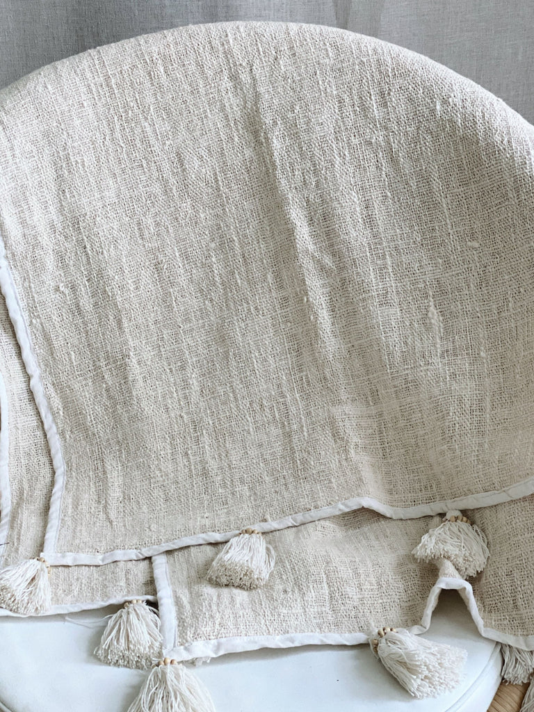 scandi bohemian jute and linen throw blanket with cream tassels over a wicker chair