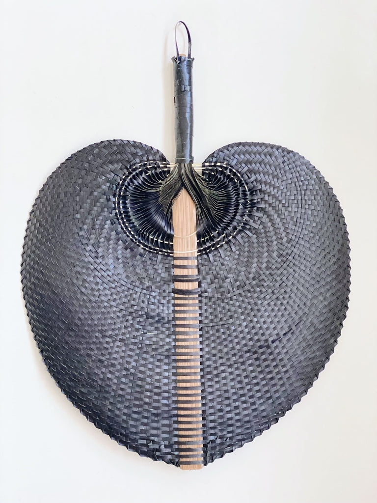 product photo of large black bohemian handwoven palm leaf fan hanging on white wall