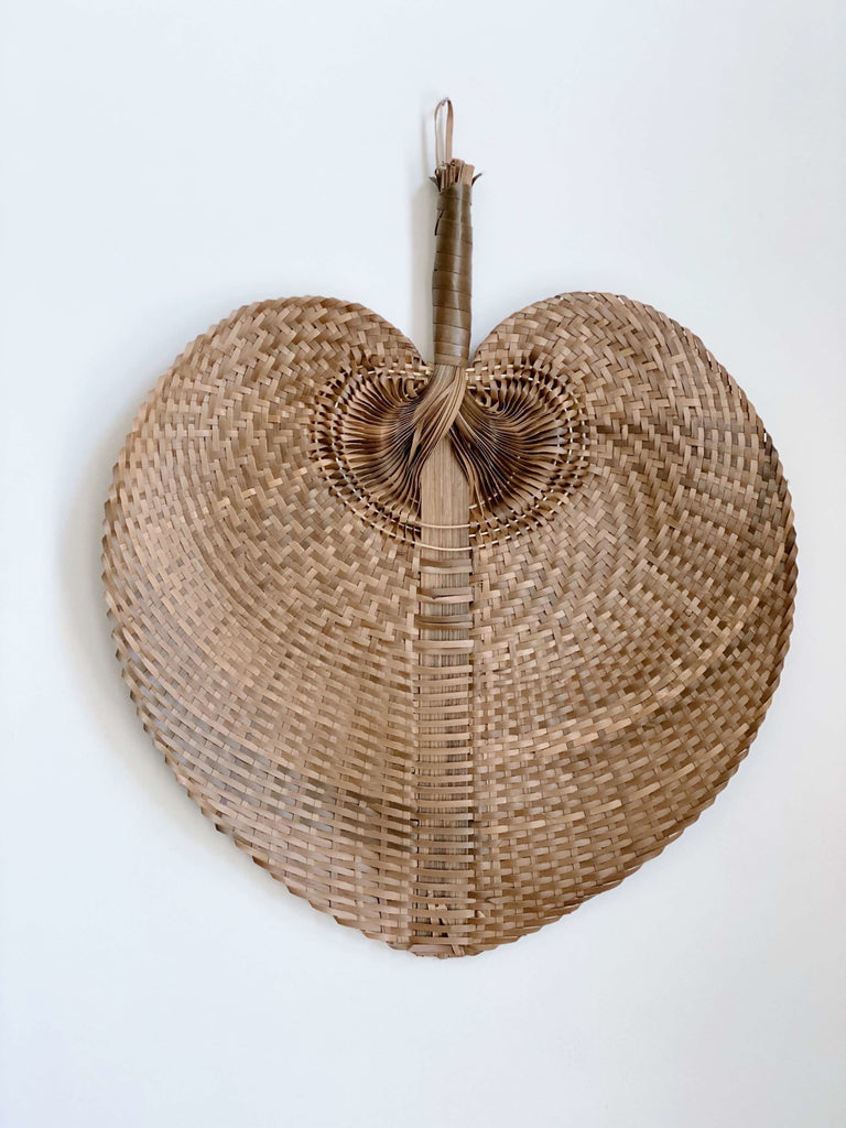 product photo of large brown bohemian handwoven palm leaf fan hanging on white wall
