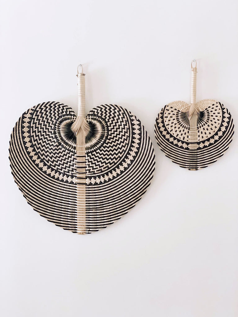 set of two large and mini natural black bohemian handwoven traditional design palm leaf fan hanging on white wall