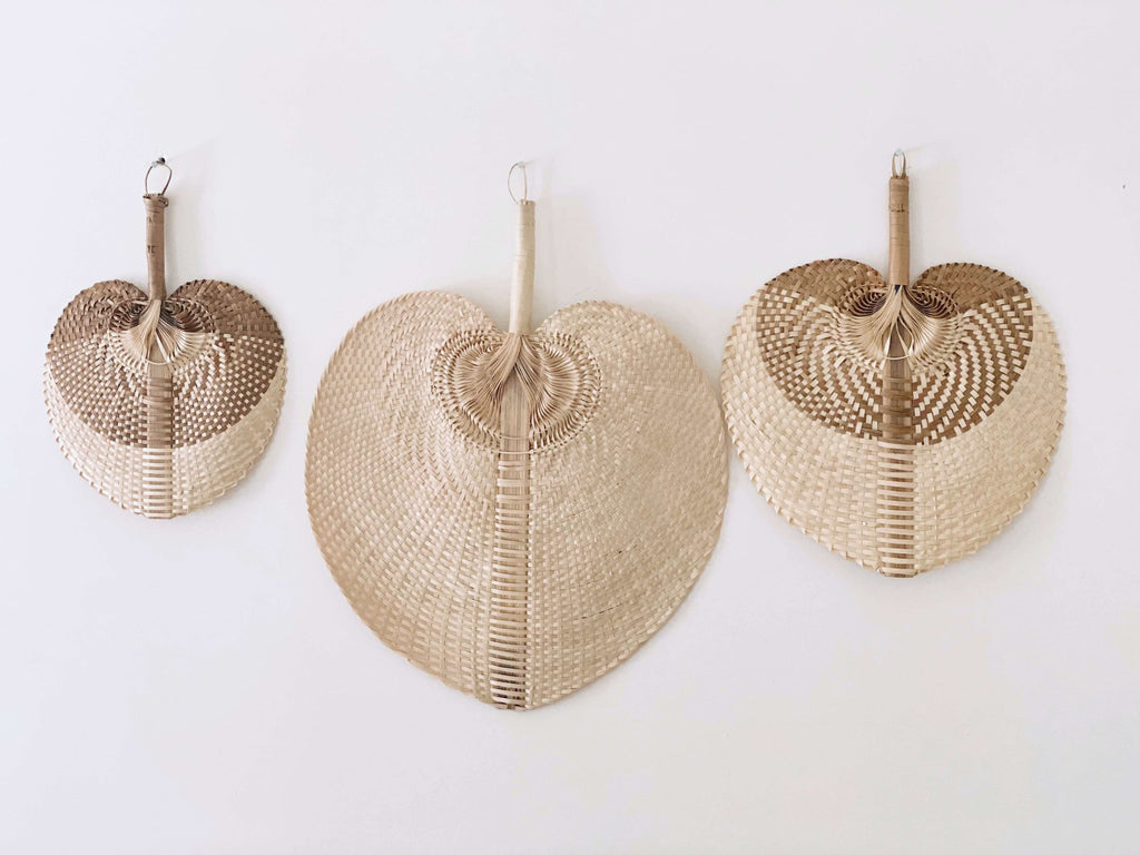 trio of small, medium, and large natural brown bohemian handwoven palm leaf fan hanging on white wall