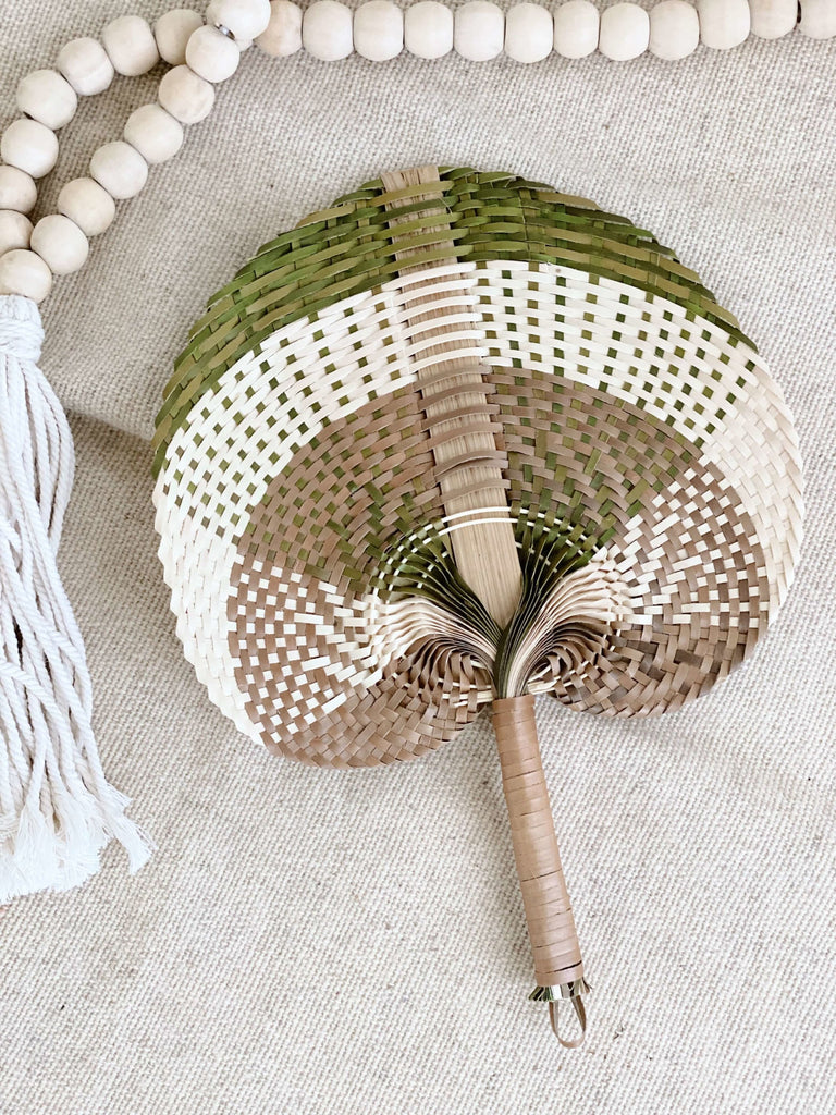 small white, brown, and olive handwoven palm leaf fan next to natural bohemian wooden bead tassel