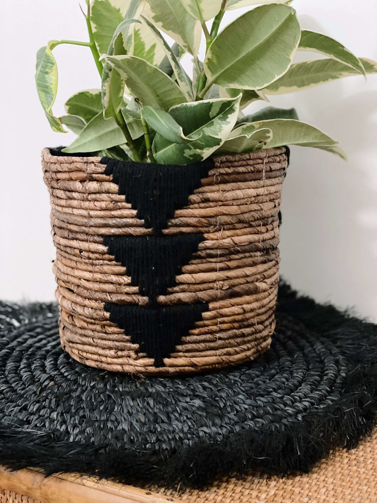 handwoven banana leaf plant basket pot with beautiful pothos plant on top of a black handmade fringe coaster