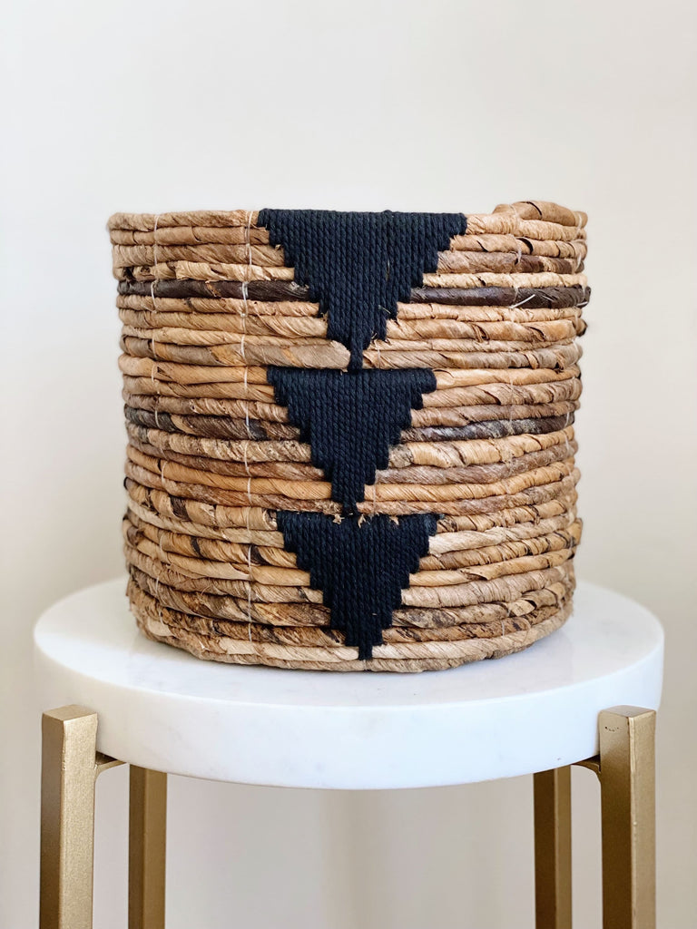 small brown handwoven banana leaf plant basket pot with black triangle design on white stool