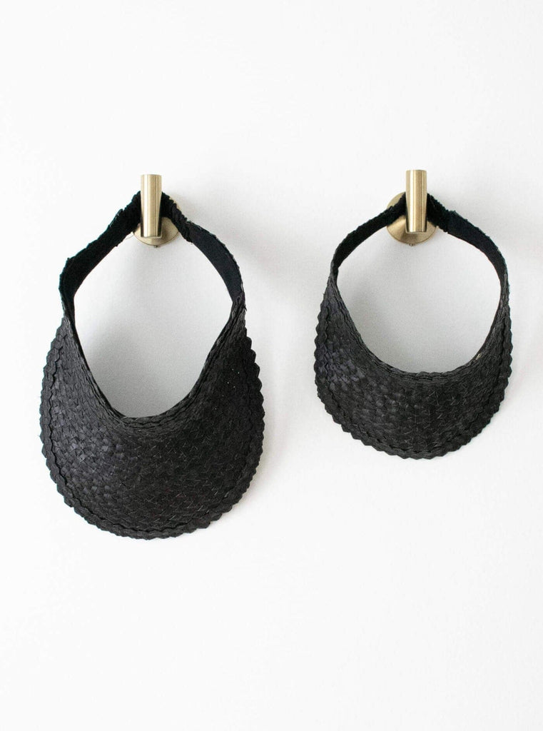 set of two regular and mini handwoven black palm leaf sun visor hanging on gold hooks on white wall
