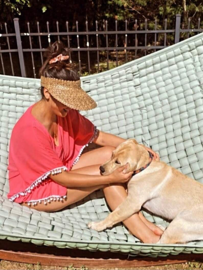 latina woman wearing palm leaf sun visor on a summer day with golden retriever on hammock