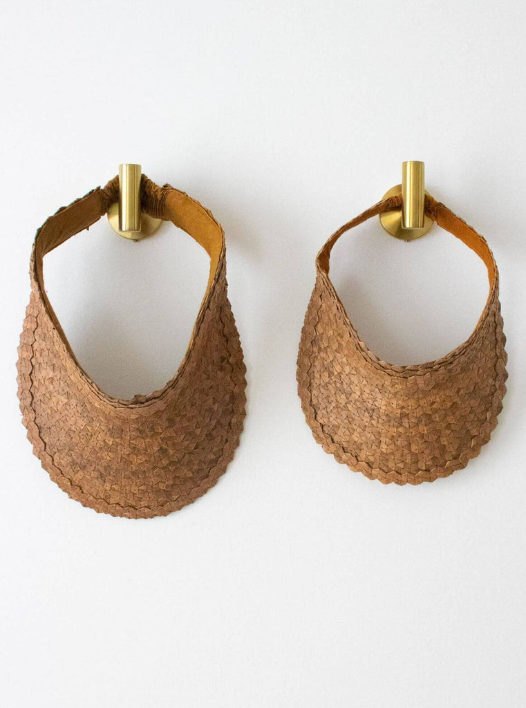 set of two regular and mini handwoven brown palm leaf sun visor hanging on gold hooks on white wall
