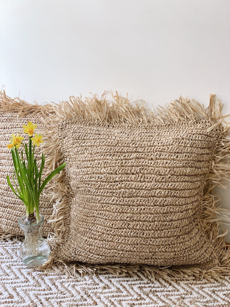 set of two handwoven bohemian raffia fringe pillows next to a beautiful vase of yellow flowers on boho rug