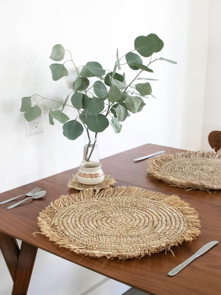 table for two in earth inspired bohemian dining room with raffia fringe placemats with a vase of eucalyptus