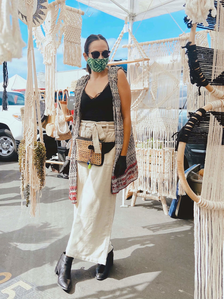 beautiful woman in bohemian fashion wearing rattan and black leather fanny pack surrounded by macrame home decor