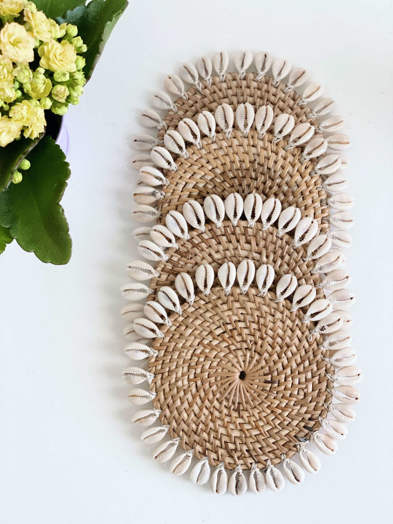 set of 4 handwoven rattan coasters adorned with white shells on white table next to beautiful yellow flowers