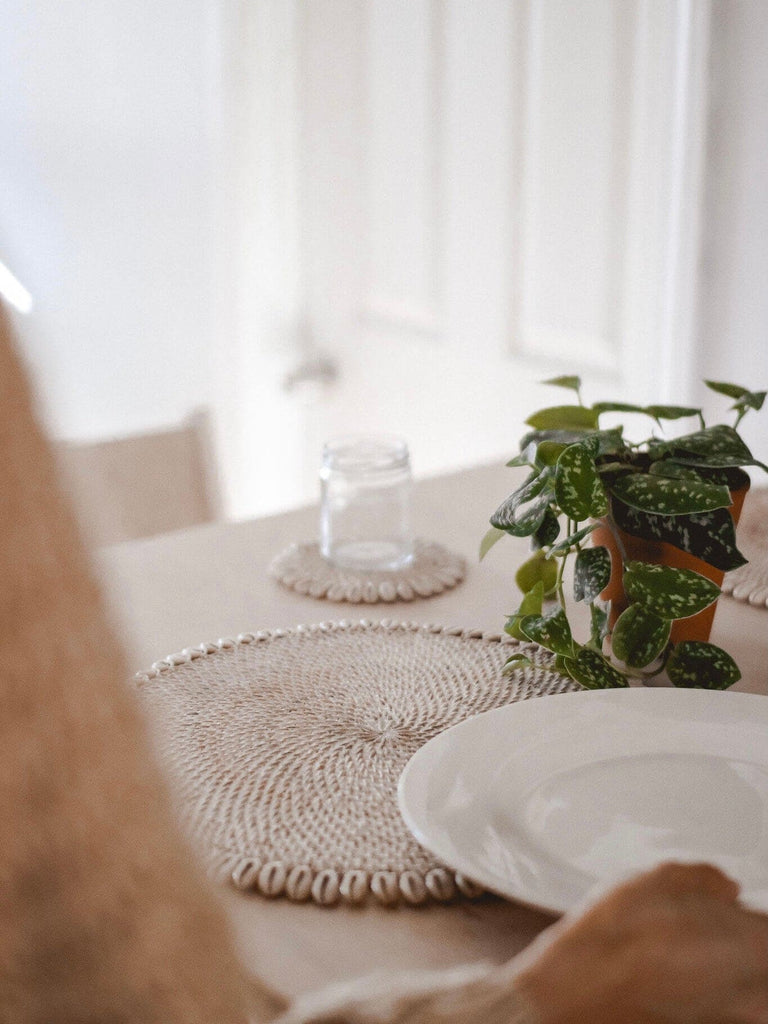 woman setting the dining table with bohemian rattan shell placemats and coaster with pothos plant centerpiece