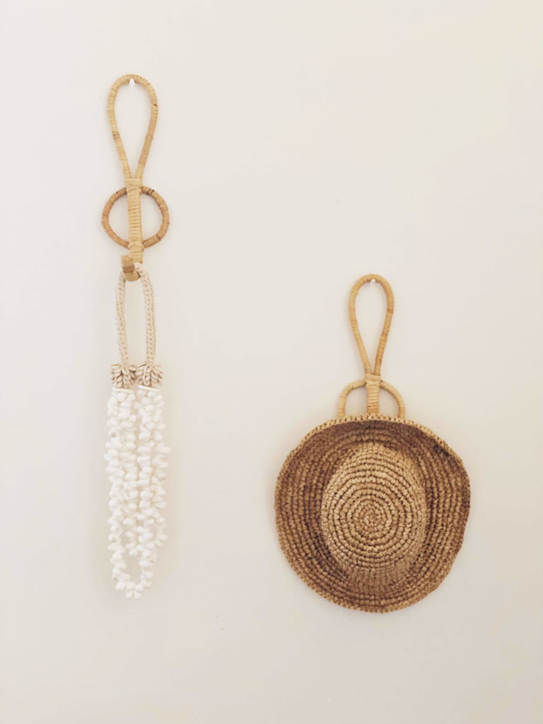 set of two wooden single hooks holding bohemian summer accessories including handwoven sun hat and shell necklace