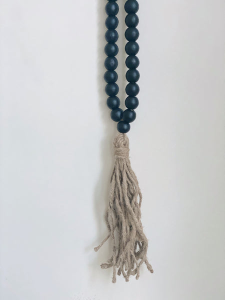 product photo of handcarved black wooden bead and jute tassel hanging on white wall