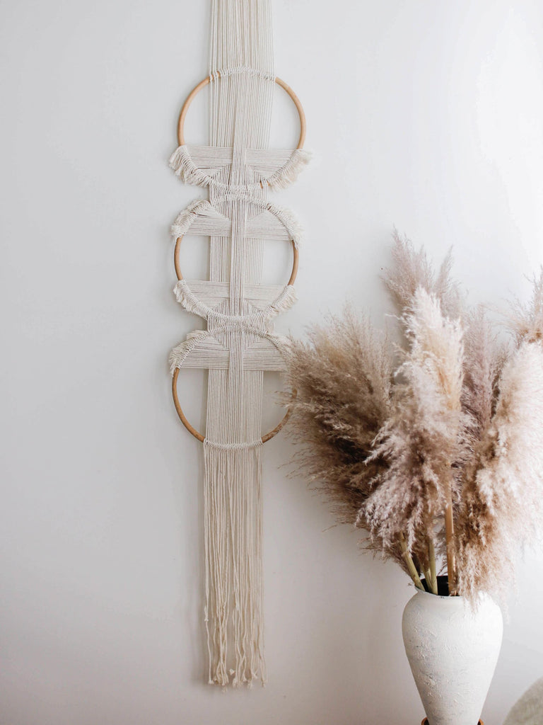 large bohemian three ring handmade cream rattan wall hanging next to a vase with pampas