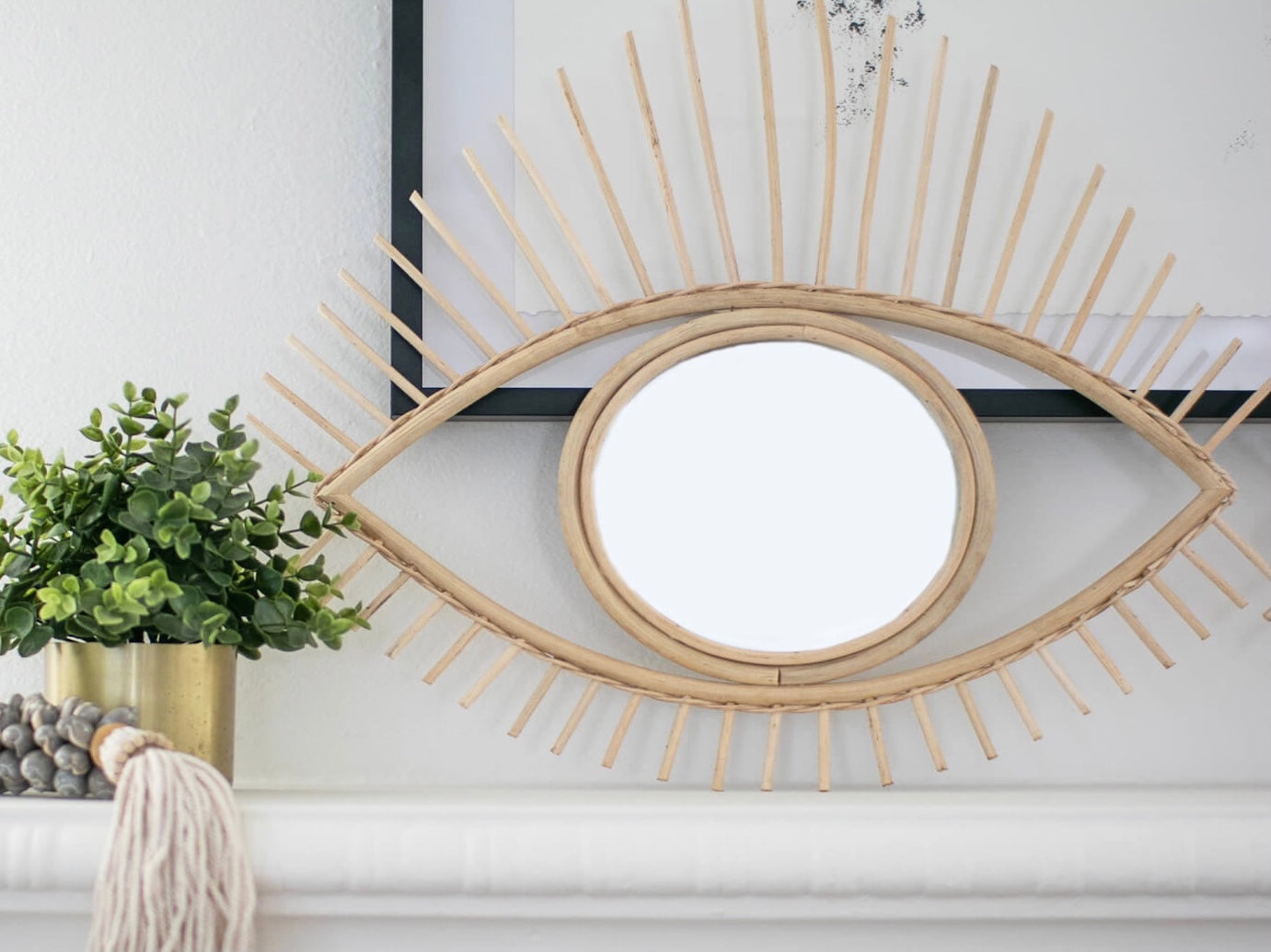 handmade rattan open eye mirror on mantel next to plant and boho decor
