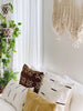 vintage african mudcloth throw pillows on a bed in a light filled bohemian bedroom with hanging plants in the background
