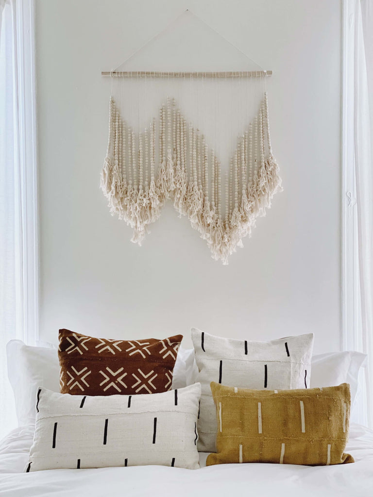 vintage african mudcloth throw pillows on bed with beaded tassel hanging in a light boho bedroom