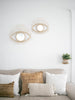 pair of open eye rattan mirrors on a wall over a gray sofa with decorative pillows in a boho chic living room