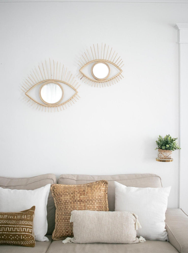 pair of open eye rattan mirrors on a wall over a gray sofa with decorative pillows in a boho chic living room
