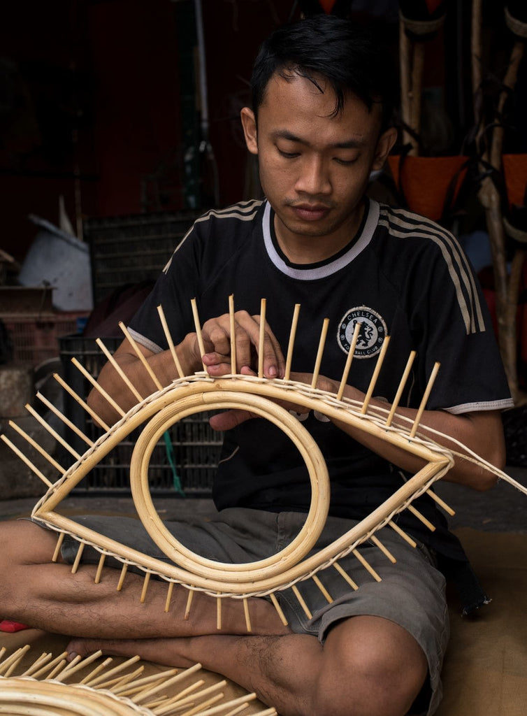 indonesian artisan crafting open eye rattan mirror inside workshop