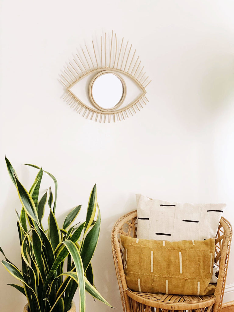 aesthetic rattan eye mirror in a boho modern room with wicker chair and vintage mudcloth throw pillows
