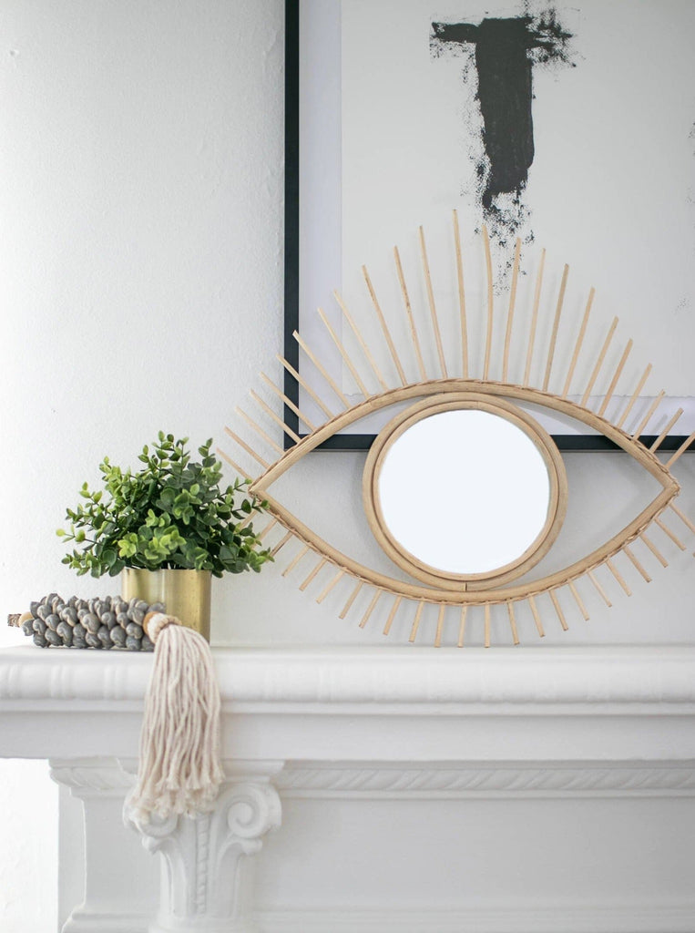 all seeing eye rattan mirror on mantel decorated with gray shell tassel and a potted plant