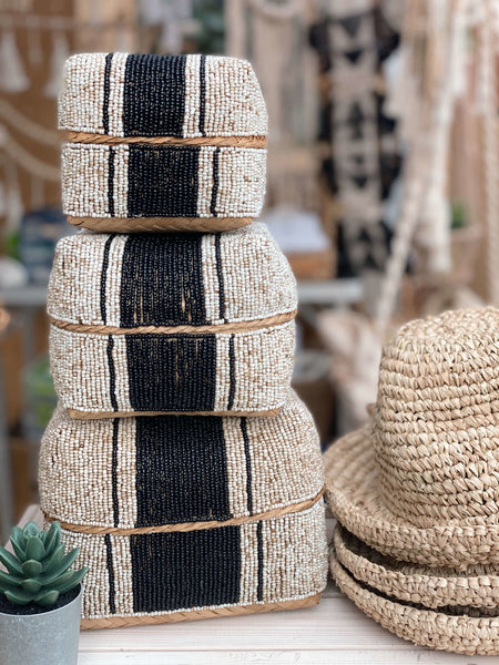 stack of three hand-beaded black and white bamboo baskets next to woven bucket hat on a white table