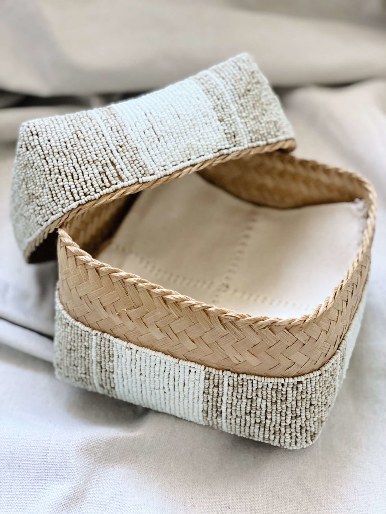 close up of tan and white handwoven beaded basket holding linen napkins