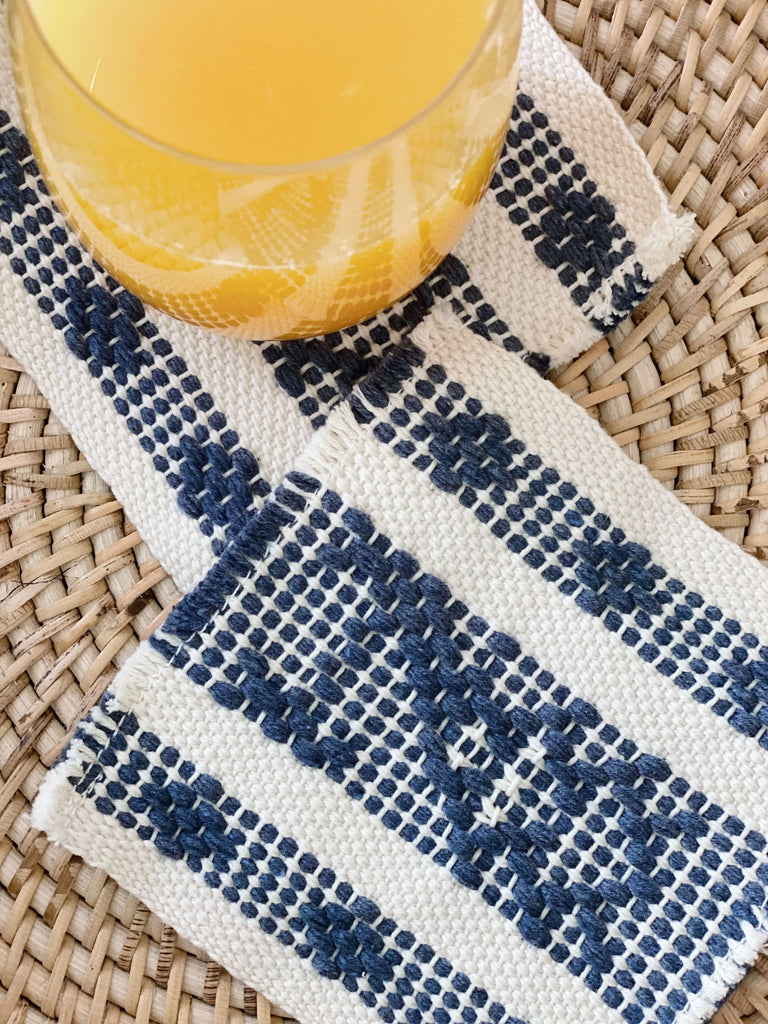 detail of waistloom embroidered coasters in cream and blue colorway with cup of orange juice in the corner of the photo