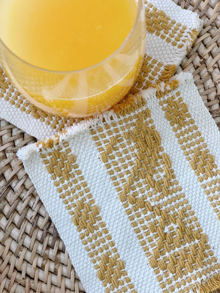 detail of waistloom embroidered coasters in cream and yellow colorway with cup of orange juice in the corner of the photo