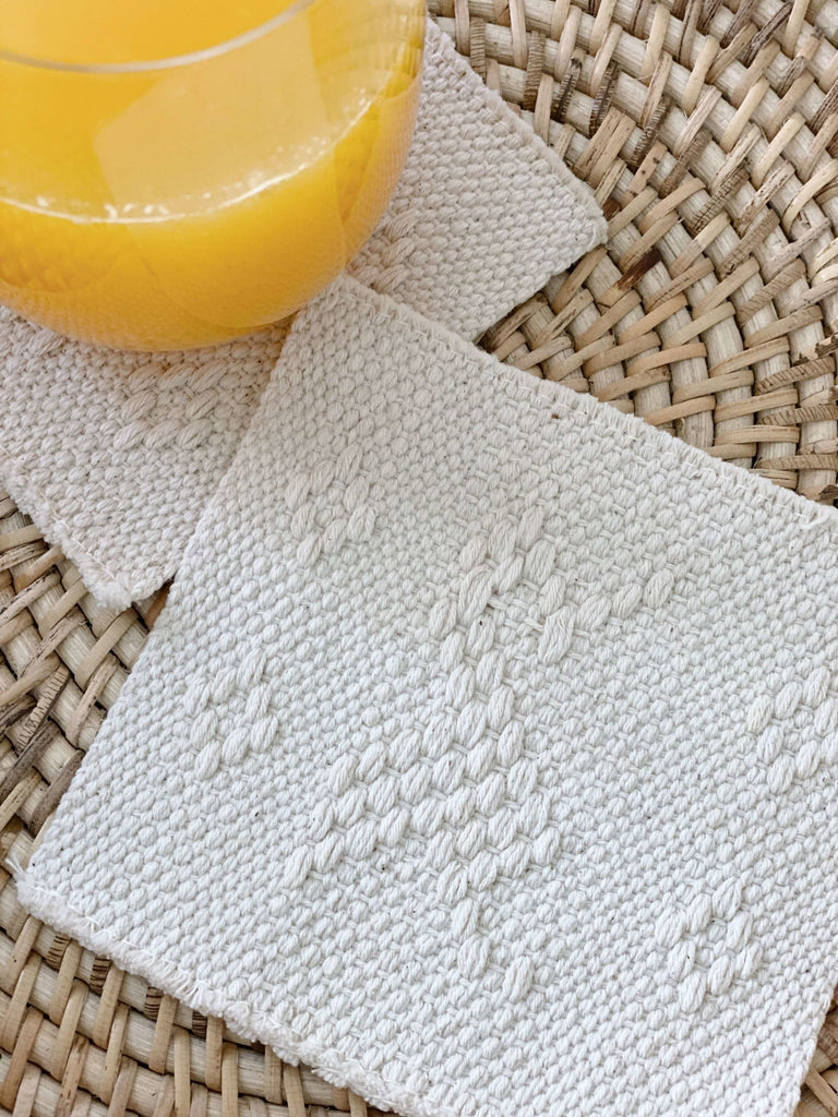 detail of waistloom embroidered coasters in cream colorway with cup of orange juice in the corner of the photo