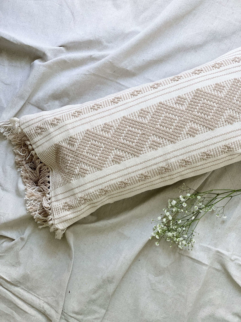 aesthetic photo of cream and taupe waistloom embroidered pillow on canvas next to baby's breath florals