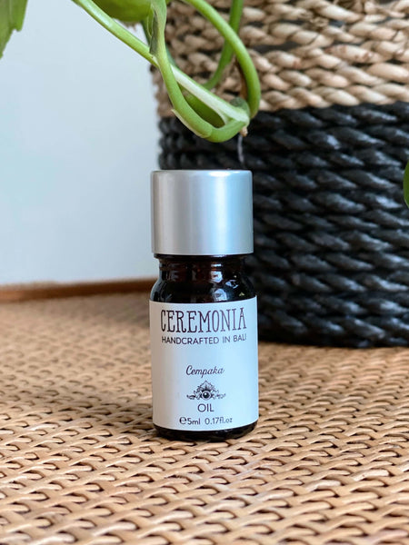 CEREMONIA cempaka essential oil in front of a black and brown woven plant pot on a wicker dresser