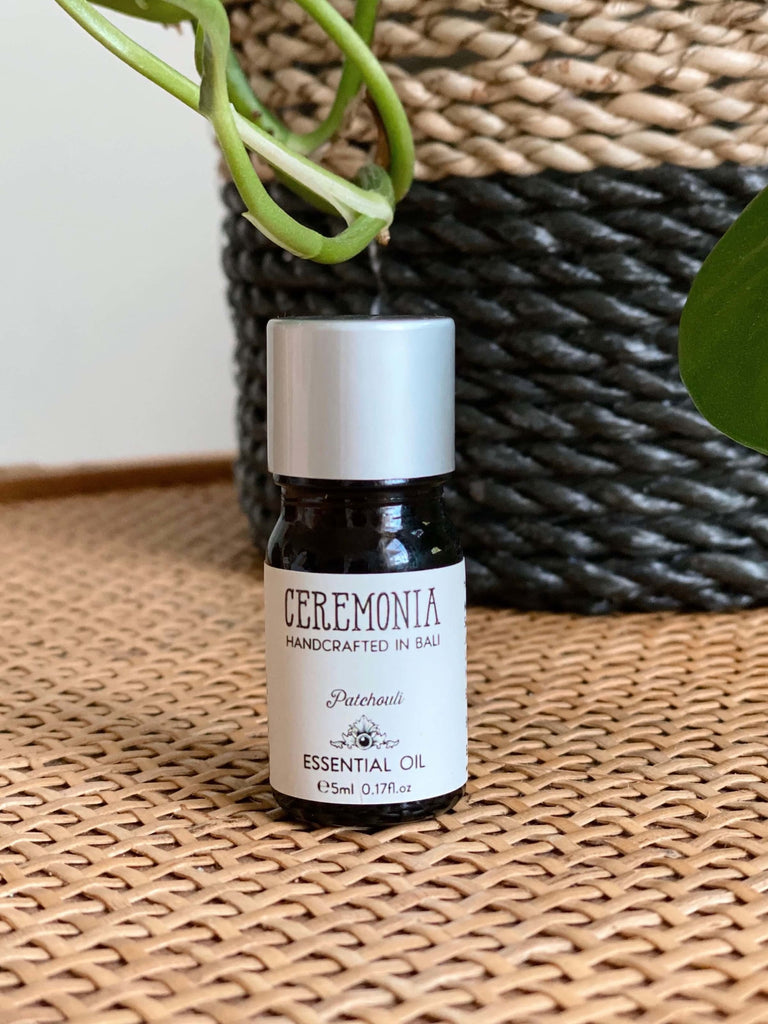 CEREMONIA patchouli essential oil in front of a black and brown woven plant pot on a wicker dresser