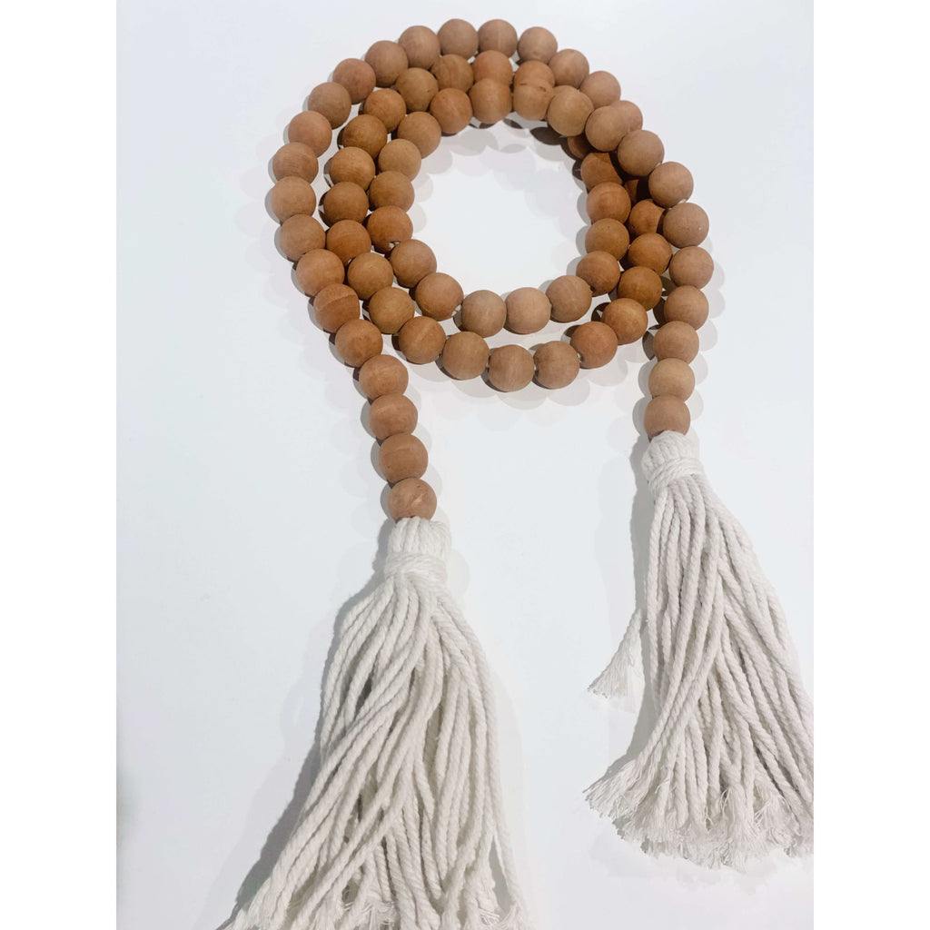brown wooden bead garland with cream tassel laid on a white surface