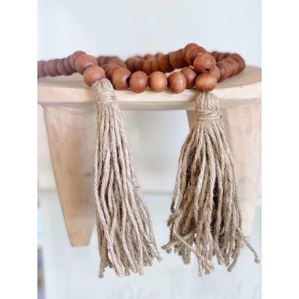 brown wooden bead garland with brown jute tassels on a wooden stool