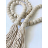 farmhouse natural wooden bead garland with cream tassels laid on a white surface creating a heart shape