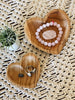 set of two heart teak dishes with pink crystal accessories and silver jewelry on a macrame surface with a potted plant