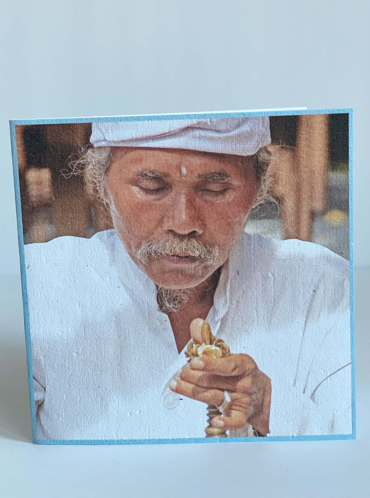 greeting card with a light blue frame and an indonesian man in traditional clothing holding a candle