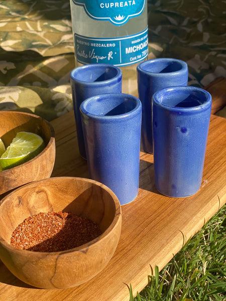 set of four blue high fire clay shot glasses with lime and chili powder in a wooden bowl on a wooden board